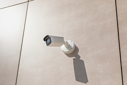 Cctv camera on wall of building in city. Surveillance and security tracking concept close-up with flare.