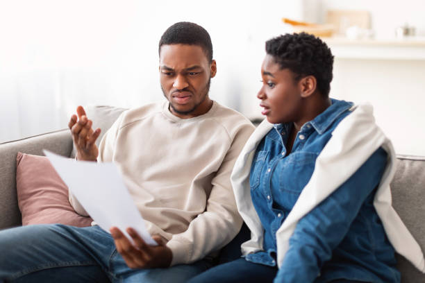 istock Confused black couple reading documentation at home, sitting on couch 1322895738
