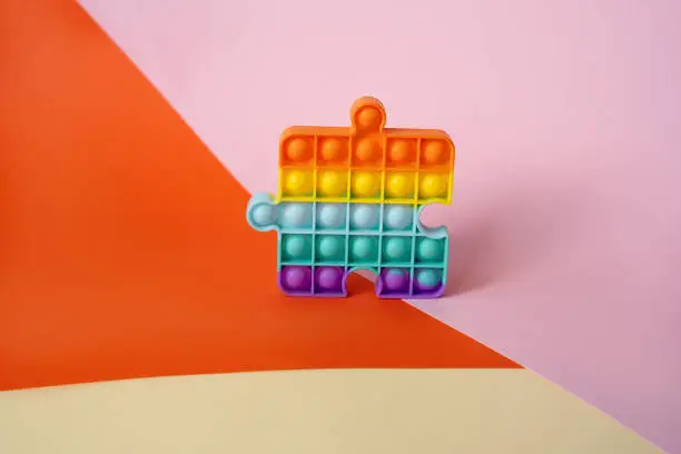 Photo of New popular silicone colorful anti-stress popit toy for baby on the background with geometric shapes.