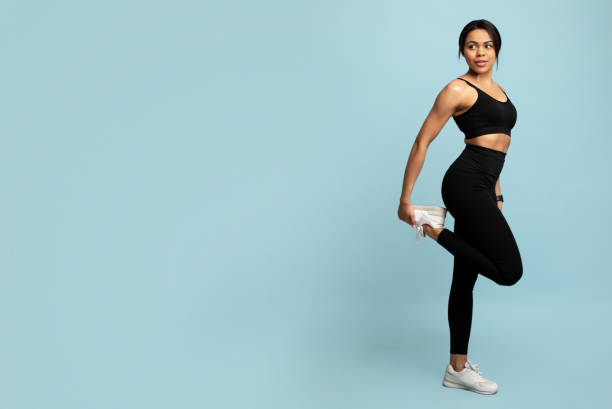 Fitness and sport concept. Young black woman stretching leg before workout, blue background with empty space Fitness and sport concept. Young black woman in sportswear stretching leg before workout, warming up, doing exercise against blue background with empty space, studio shot, banner athleticism photos stock pictures, royalty-free photos & images