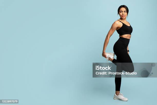 Fitness And Sport Concept Young Black Woman Stretching Leg Before Workout Blue Background With Empty Space Stock Photo - Download Image Now