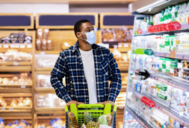 istock Young black guy in disposable face mask selecting dairy products at store during covid quarantine 1322897188