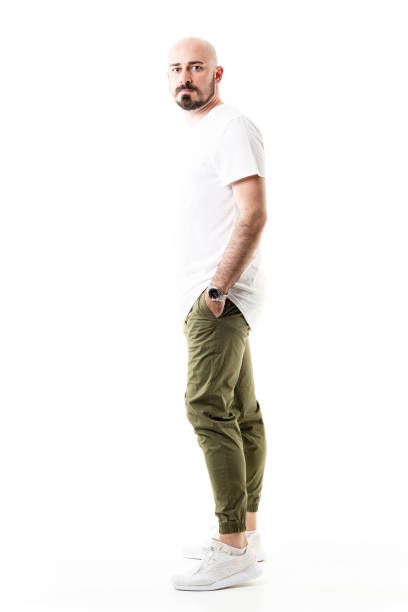 Side view of standing young bald shaven man in chino trousers Side view of standing young bald shaven man in chino trousers. Full body length isolated on white background olive green shirt stock pictures, royalty-free photos & images