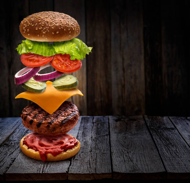 istock Burger layered ingredients as explosion flying open bun on rustic wooden table 1322898458
