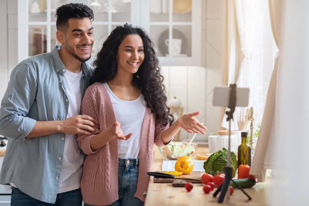 istock Young Arab Couple Using Smartphone On Tripod In Kitchen For Recording Vlog 1322898772