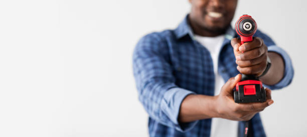 istock Black man holding screwdriver like gun and aiming at camera, white background, panorama with copy space 1322900093
