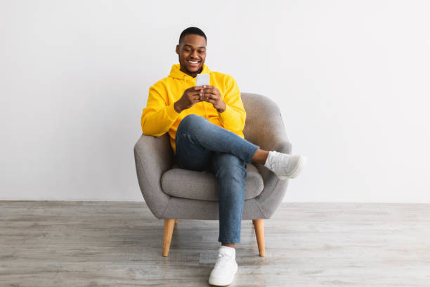 istock African Guy Using Smartphone Sitting In Chair Over Gray Wall 1322900709