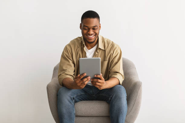 istock Black Guy Using Tablet Sitting In Chair Over Gray Background 1322900711