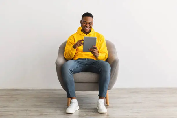 Photo of Happy Black Guy Using Digital Tablet Browsing Internet, Gray Background