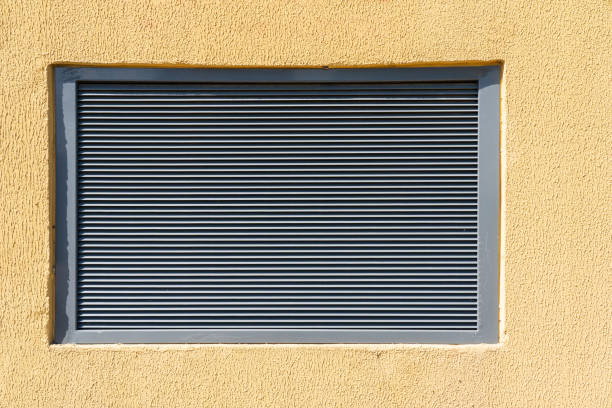 una finestra di metallo grigio in un muro di pietra gialla. c'è una griglia di ventilazione louvred. sfondo. trama. - louvred foto e immagini stock