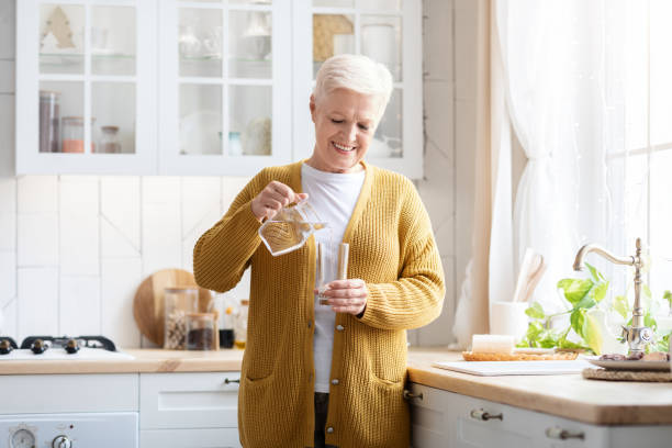istock Senior woman pouring water into glass, kitchen interior 1322902036