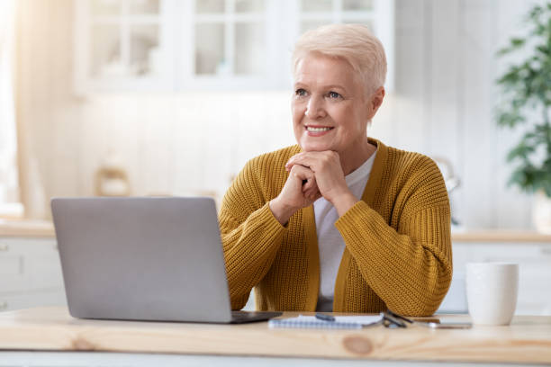 istock Happy old lady working on laptop at home, kitchen interior 1322902050