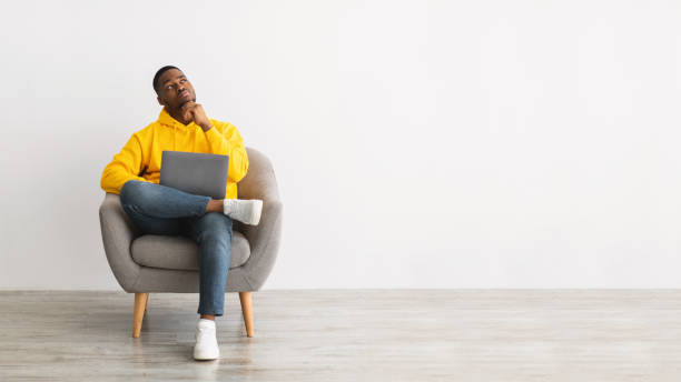 istock African Guy With Laptop Thinking Sitting In Chair, Gray Background 1322905008