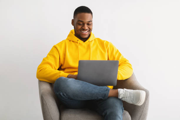 istock Happy African Guy Using Laptop Sitting In Chair, Gray Background 1322905059