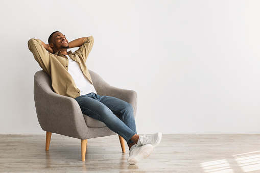 Weekend. Happy African American Man Relaxing Sitting In Chair Holding Hands Behind Head Posing With Eyes Closed On Gray Wall Background, Enjoying Silence And Comfort Of Minimalism Lifestyle