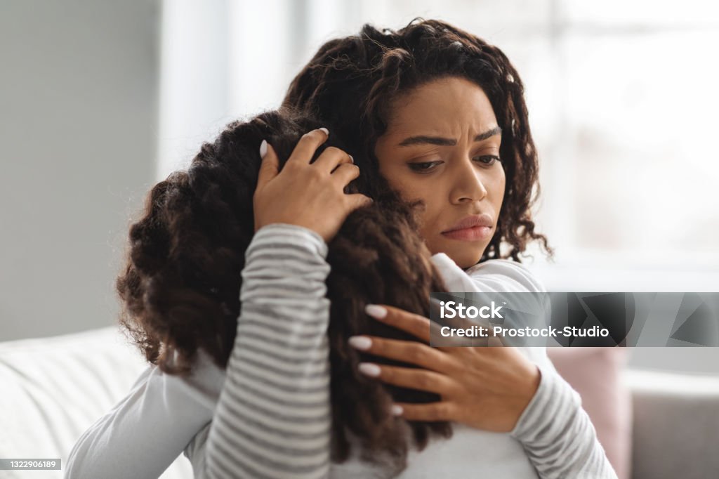 Young black mother comforting her crying daughter Young black mother comforting her crying daughter, hugging her and whispering words of support, closeup. African american woman embracing female kid, touching her head and saying something Crying Stock Photo
