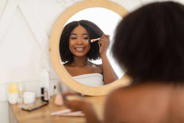 istock Attractive black lady applying decorative makeup in front of mirror, sitting at dressing table indoors 1322906388