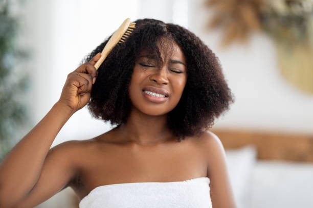 frustrierte tausendjährige schwarze frau versucht, ihre verworrenen haare zu hause zu bürsten. hausfriseur-konzept - frizzy hairstyle human hair women stock-fotos und bilder