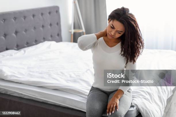 Portrait Of Black Woman With Neck Pain Sitting On Bed Stock Photo - Download Image Now