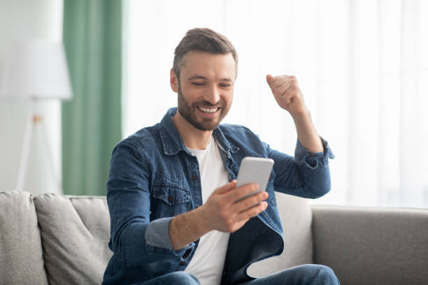 istock Emotional bearded man celebrating success, using mobile phone 1322908641