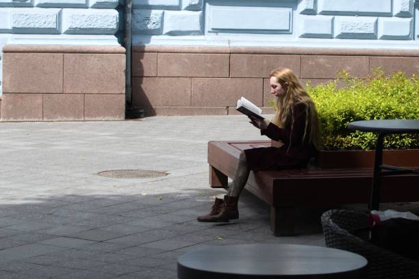 Occasional photo on the street. Girl reads book sitting at the bench on city street. Ukraine Zhytomyr 10 June 2021