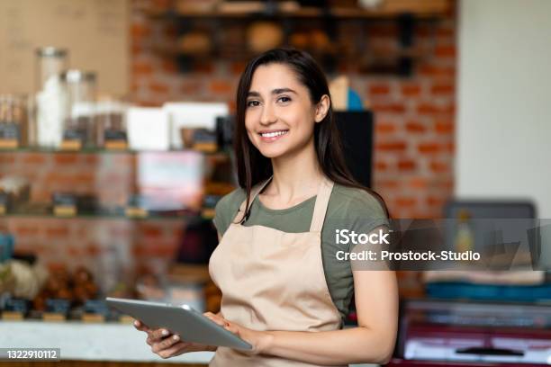 Opening Small Business Happy Arab Woman In Apron Near Bar Counter Holding Digital Tablet And Looking At Camera Stock Photo - Download Image Now