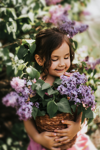 Little girl holding basket with blooming lilacs.