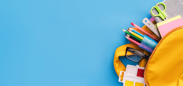 School supplies sticking out of backpack on blue background School supplies sticking out of backpack on blue background. classroom empty education desk stock pictures, royalty-free photos & images