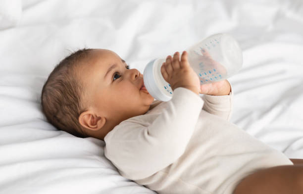 istock Cute little black baby drinking from bottle lying in bed 1322911270