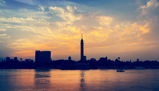 Cityscape of Cairo downtown at sunset with silhouettes of Cairo Tower at horizon. Romantic evening cruise on Nile River - skyline from an embankment of modern Cairo.