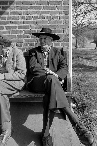 Silva, Jackson County, North Carolina, USA - March 15, 1982: Residents of the Jackson County Home sit outside on a bench on a Spring afternoon in Silva, North Carolina. The Jackson County Home was built in 1924 and provided a home for both men and women who were going through difficult times. Through many years, the home was self-sufficient as residents (who were referred to as inmates) worked in the vegetable gardens, milked cows and kept pigs and chickens for meat and eggs. In the later years, struggles with funding continued and the facility shut down and was demolished in 1986.