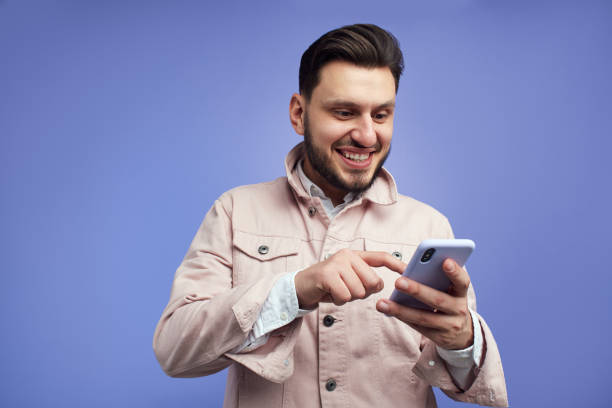 istock Young cheerful excited man using smartphone, isolated over blue background 1322911569