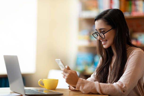 istock Freelance concept. Happy arab woman working on pc at cafe, drinking tea and using smartphone, having break 1322911618