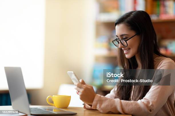 Freelance Concept Happy Arab Woman Working On Pc At Cafe Drinking Tea And Using Smartphone Having Break Stock Photo - Download Image Now