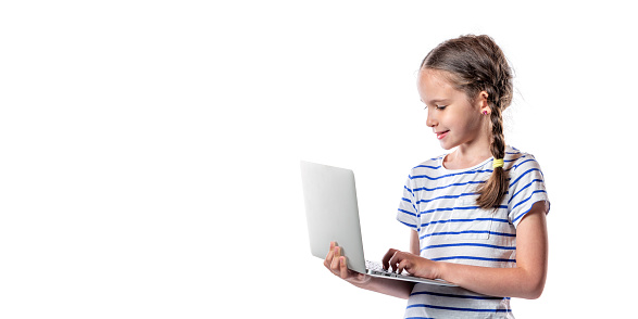 Cute little european girl holding and working with modern silver laptop isolated on white background. Free space.