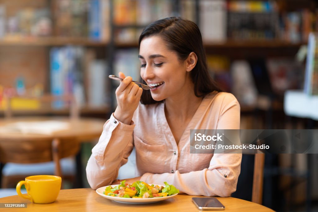 Happy latin woman eating lunch in cafe, enjoying delicious salad with closed eyes and drinking hot beverage Happy latin woman eating lunch in cafe, enjoying delicious salad with closed eyes and drinking hot beverage. Lady eating healthy meal, sitting indoors in restaurant, free space Healthy Eating Stock Photo
