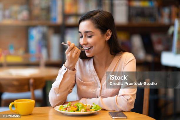 Happy Latin Woman Eating Lunch In Cafe Enjoying Delicious Salad With Closed Eyes And Drinking Hot Beverage Stock Photo - Download Image Now