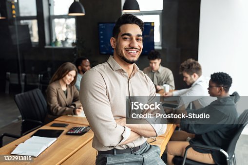 istock Young bearded businessman sitting on desk and posing 1322913815