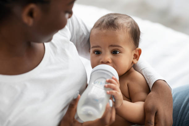 African American lady feeding her child from baby bottle Childcare Concept. Closeup portrait of happy African American woman holding baby bottle and feeding her cute little black with milk at home. Nutrition, Love, Care And Family, Babysitting suckling stock pictures, royalty-free photos & images