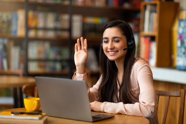istock Excited latin lady having video call while resting at cafe, using laptop and headphones, copy space 1322913936