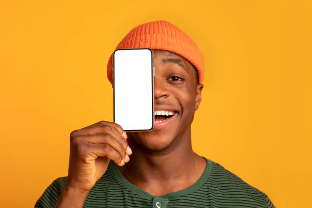 istock Cheerful Black Hipster Guy Covering Face With Smartphone With Blank White Screen 1322915794