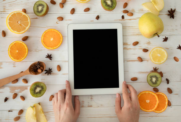 istock Healthy nutrition concept. Female hands holding digital tablet with black screen on table with fruit slices, top view 1322915856