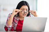視力の問題。ラップトップ画面を見ながら眼鏡を脱ぐアジアの女性