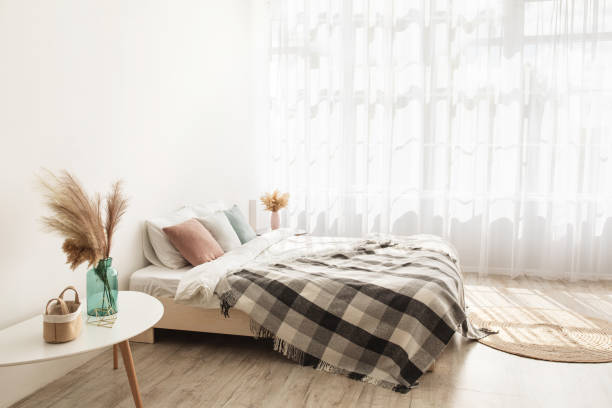 istock Light boho style and real estate design. Bed with pillows and blanket, carpet, tables with dry plants in vases 1322916815