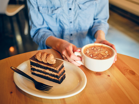 A woman sitting at a table with a cafe latte and chocolate cake.