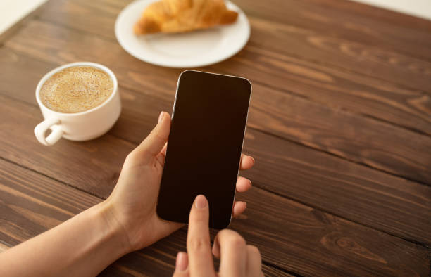 istock Cool app. Woman using smartphone with black screen and drinking coffee at cafe, closeup 1322918626