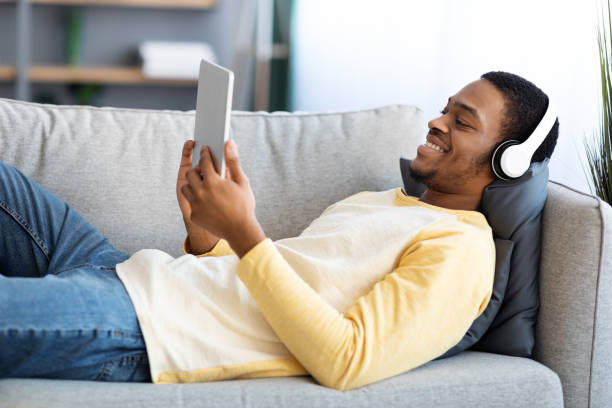 istock Smiling black guy laying on couch, watching movies on pad 1322918902