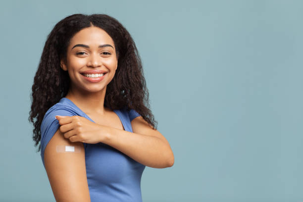 ich habe meinen covid-19-impfstoff bekommen. glückliche afrikanische amerikanische dame zeigt geimpften arm nach antiviraler injektion, blauer hintergrund - verputz fotos stock-fotos und bilder