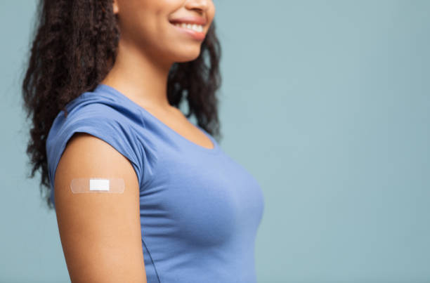 istock Vaccination concept. Happy unrecognizable black lady showing vaccinated arm with plaster, blue background, free space 1322918920