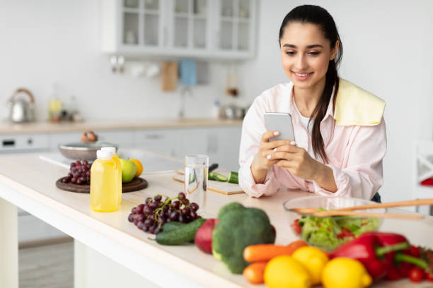 istock Portrait of smiling young lady using cellphone in kitchen 1322919985